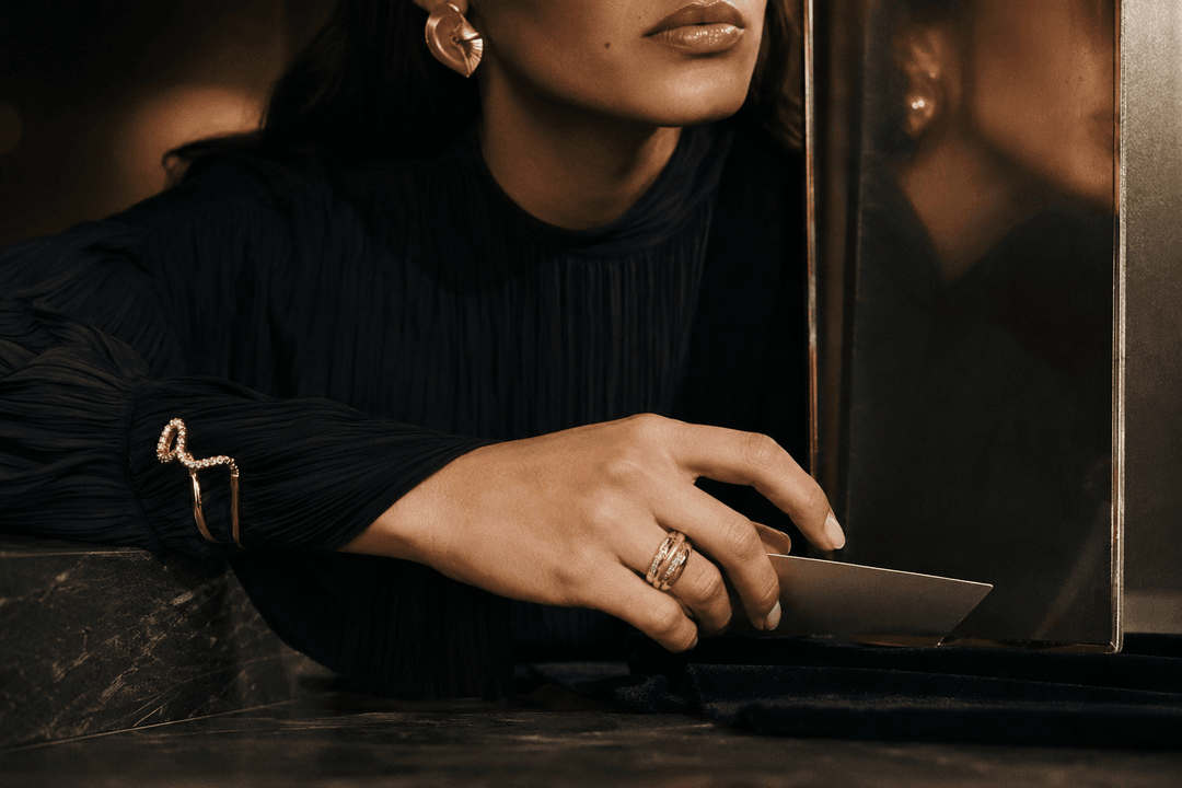 Adult Latina model’s hand in motion wearing a sculptural statement ring, with a quieter cuff and an architectural earring visible in the composition.
