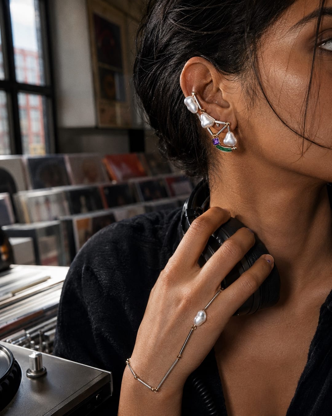 South Asian model at a record-shop listening station wearing a three-pearl titanium ear talisman and a fine pearl hand ornament