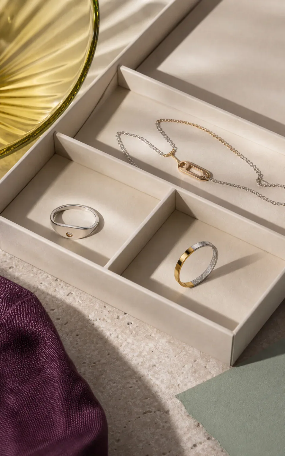 Mixed-metal rings and a necklace arranged in separate compartments of an open jewelry box