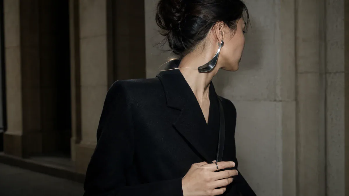 Adult wearer in a dark architectural coat with an original sculptural ear concept under hard flash