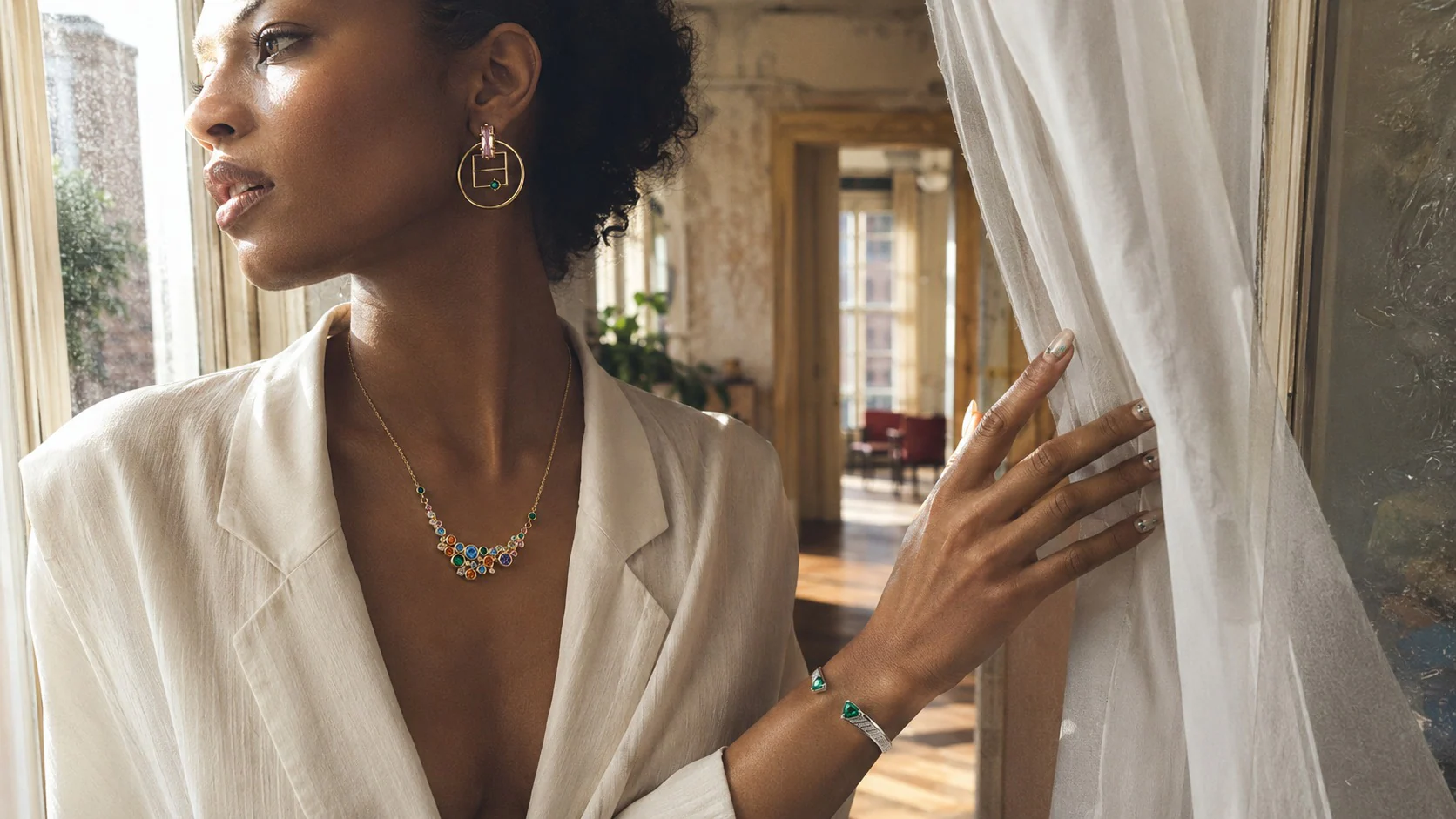 Black fashion model in a sunlit New York apartment wearing Switchroom gemstone jewelry and an editorial manicure