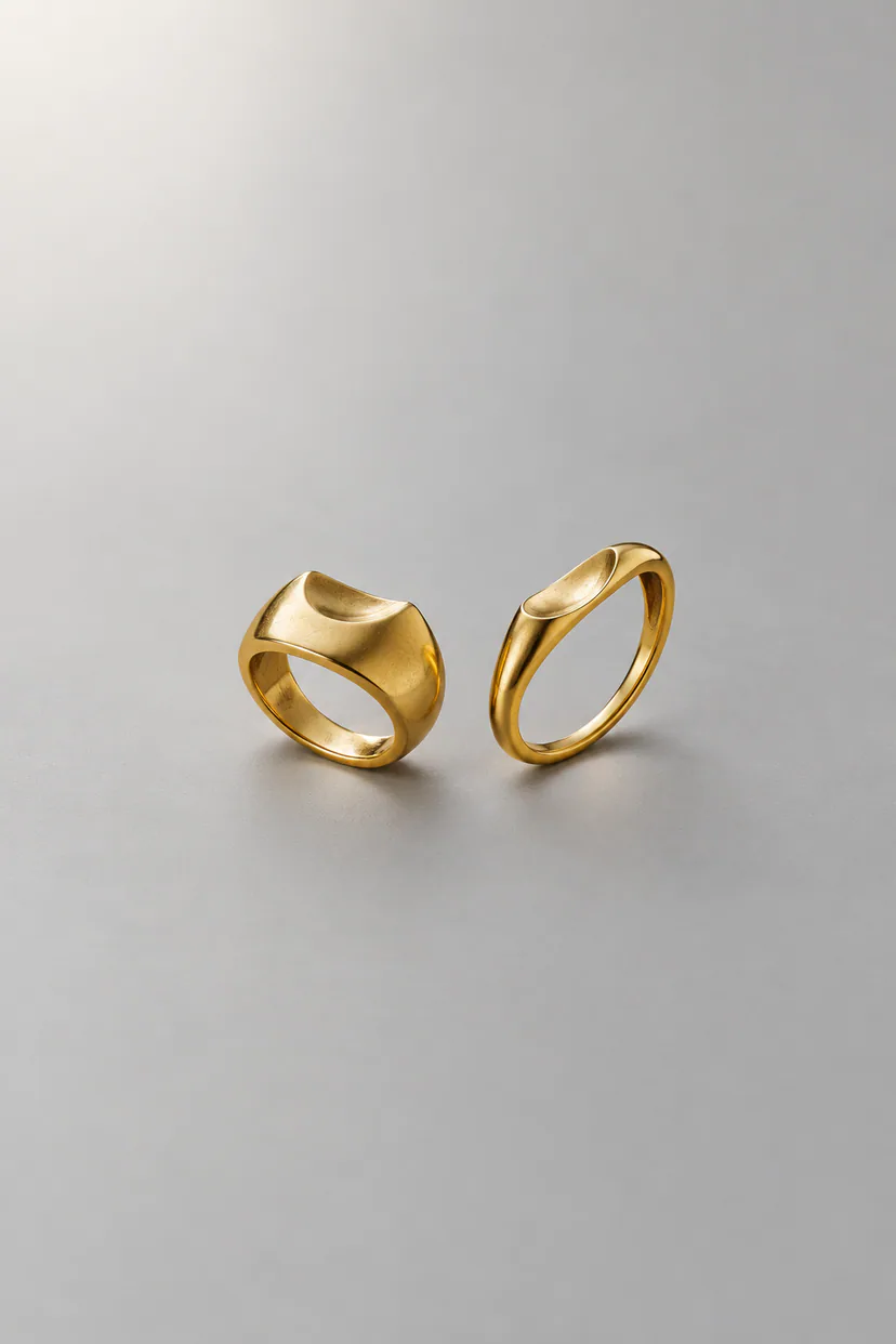 Two fictional ring forms with different silhouettes and concave upper curves, arranged side by side on softly lit gray ground.