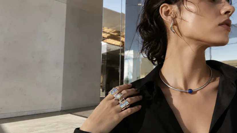Adult wearer styling sculptural silver rings, earrings, and a collar necklace in an architectural setting