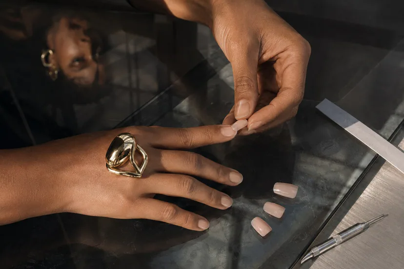 Latina model dry-fits a short press-on from sidewall to sidewall while wearing a polished dome ring over a smoked-glass measurement surface.