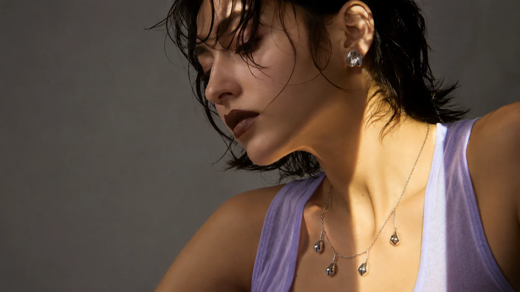 Adult model wearing a sculptural silver necklace and earrings in a jewelry-led editorial portrait