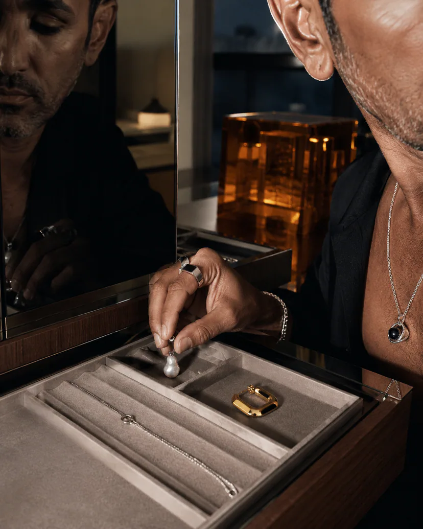Adult wearer separating a pearl pendant and mixed-material jewelry on a padded storage tray