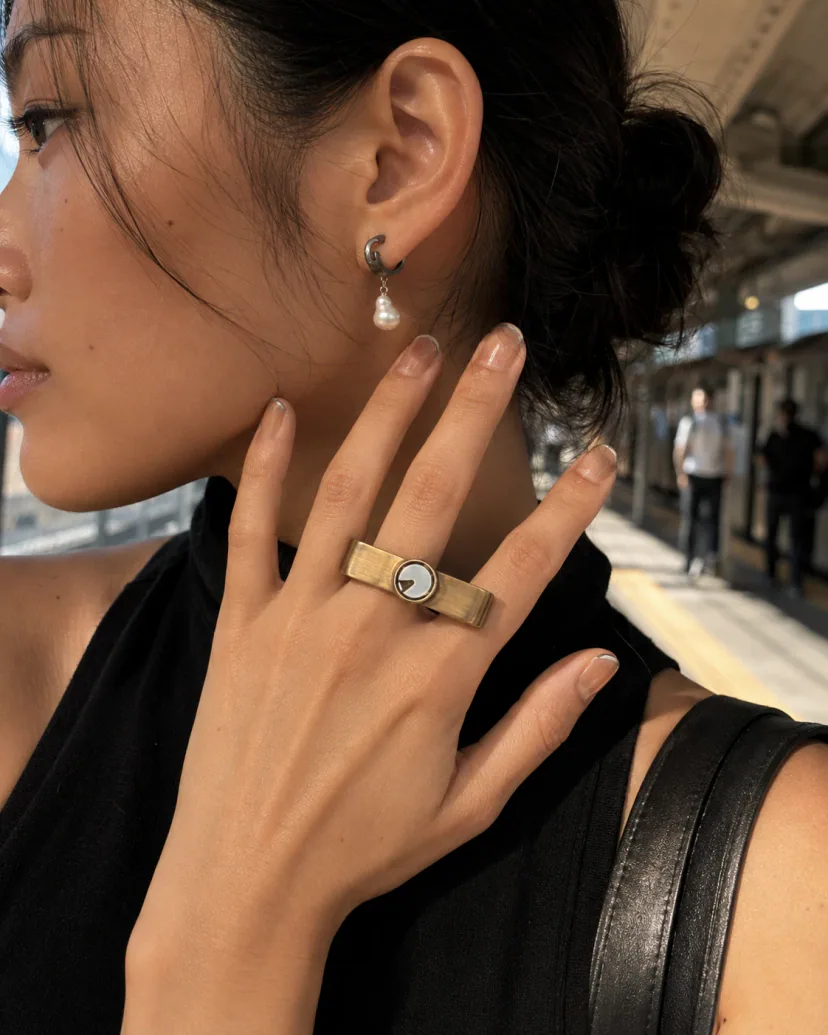 Half-profile of an adult model touching a striped ceramic ring while wearing a pearl ear loop