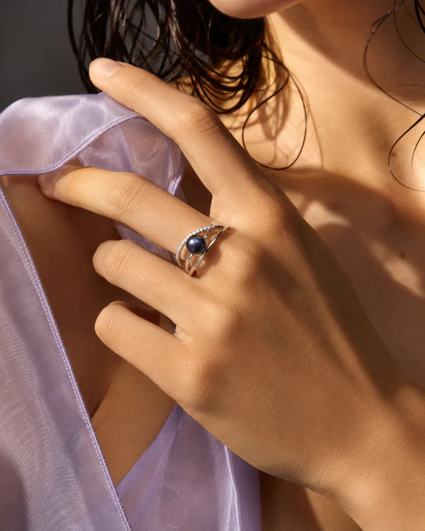 Midnight-toned pearl crossover ring with polished silver-tone band and clear-stone pavé arc