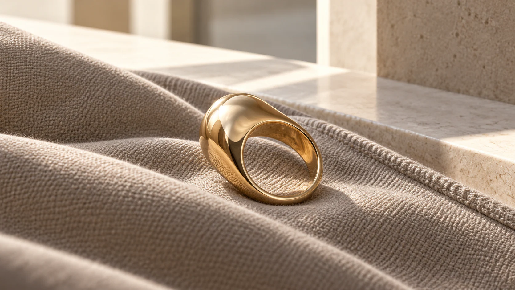 Original editorial concept of an unworn sculptural ring resting in folded cloth beside a sunlit architectural threshold.