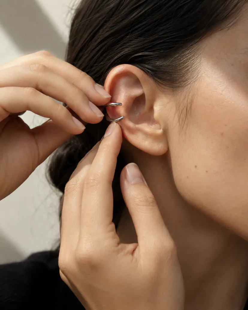 How to put on an ear cuff: adult hands position a silver-tone cuff at the thin outer edge of the upper ear.