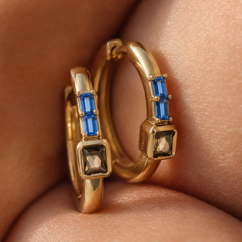 Macro detail of Switchroom gold hoop earrings with blue baguettes and smoky square stones