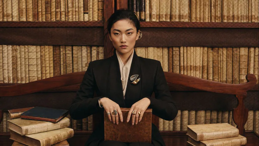 Adult wearer styling sculptural rings, a brooch, and an ear cuff in a library setting