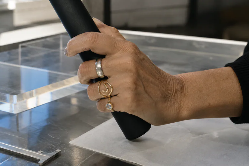Close view of an older adult hand gripping a black cylinder while wearing one broad silver ring, one fluid gold ring and a clear stone ring.