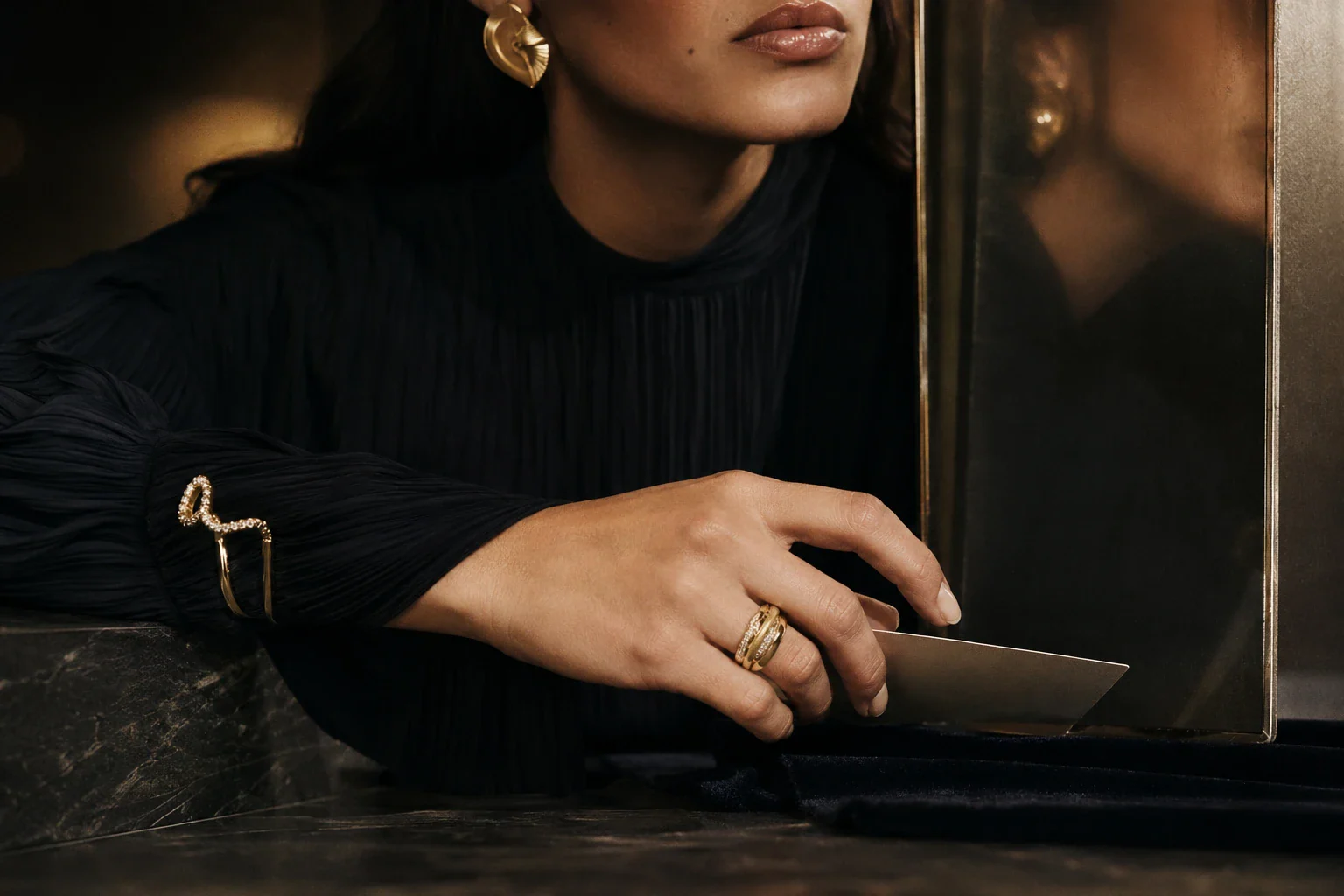 Adult Latina model’s hand in motion wearing a sculptural statement ring, with a quieter cuff and an architectural earring visible in the composition.