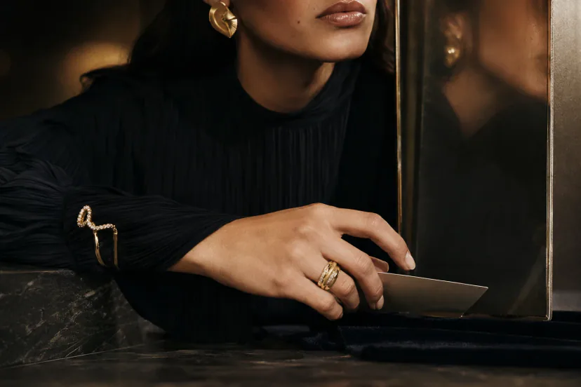 Adult Latina model’s hand in motion wearing a sculptural statement ring, with a quieter cuff and an architectural earring visible in the composition.