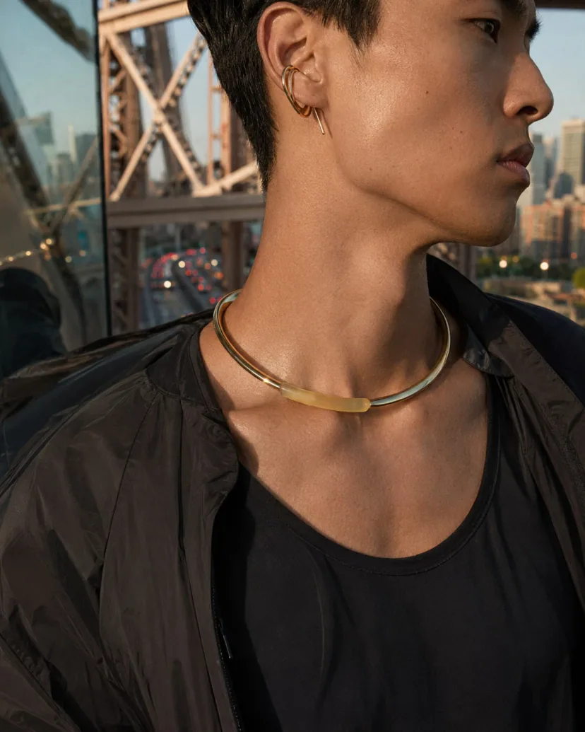 Adult East Asian man on an elevated city bridge wearing a metal ear form and collar with one translucent color accent.