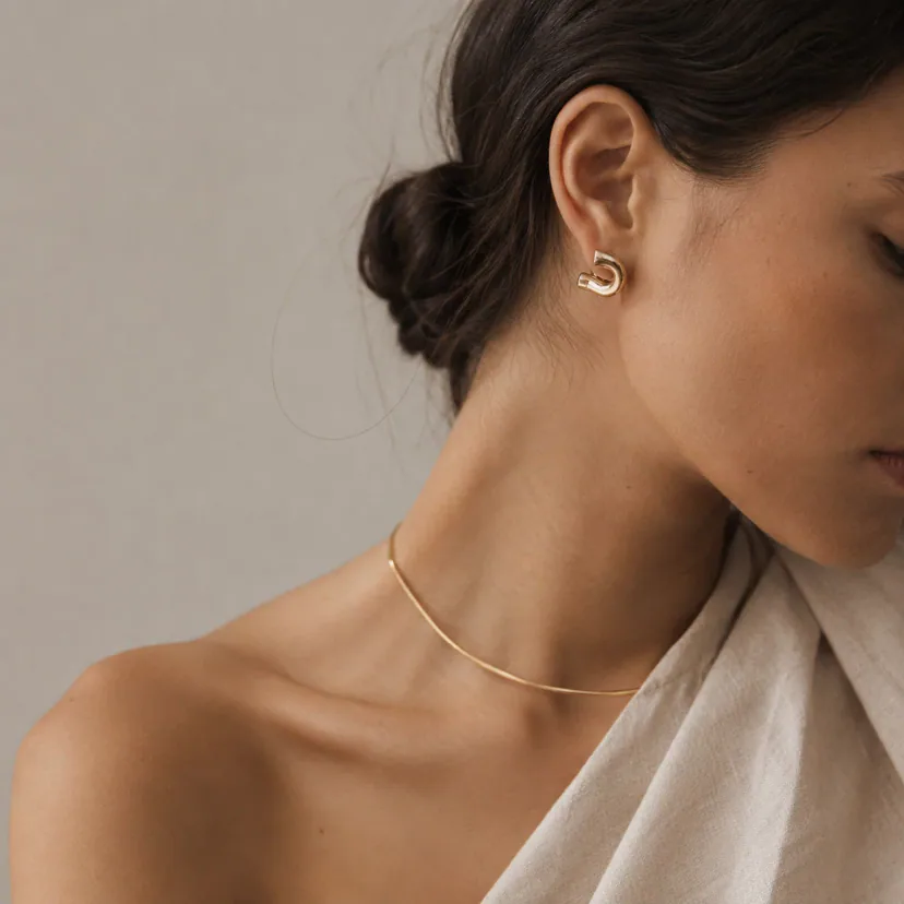 Adult model naturally wearing sculptural earrings and a fine necklace in a close editorial portrait