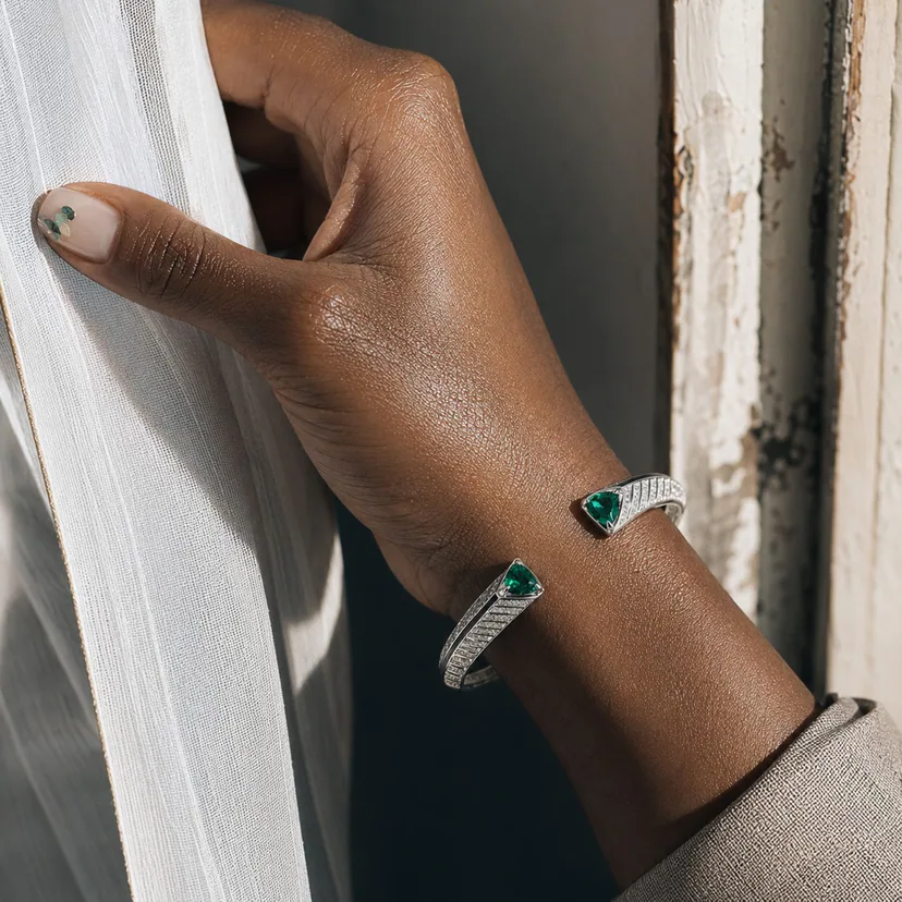 Macro of a Switchroom silver emerald open cuff and subtle gemstone manicure against a sunlit curtain