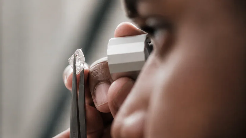 Gemologist examining a rough translucent diamond with tweezers and a jeweler's loupe.