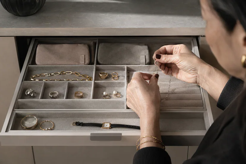 Adult hands placing a chain into a three-zone jewelry organizer with ring, earring, and necklace sections