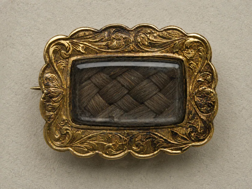 Victorian mourning brooch with braided hair beneath glass in an engraved gold-tone frame
