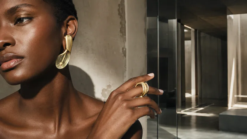 Adult Black model wearing a sculptural metal-and-translucent earring and a statement ring in an architectural close crop.